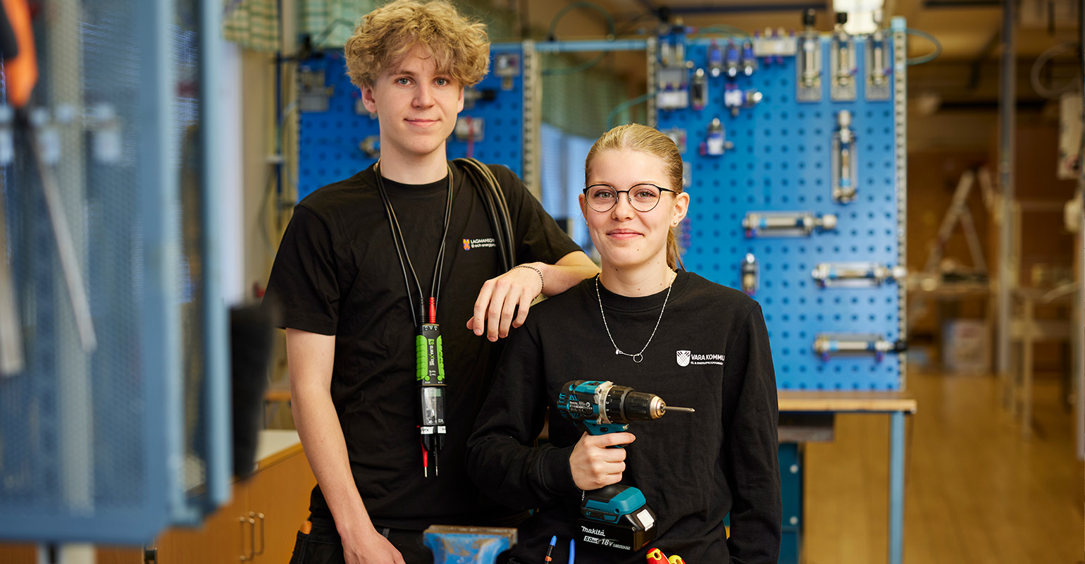 Två elever som står i elsalen och håller i olika elinstrument. 