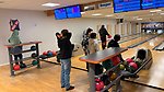 Tre barn och tre vuxna, fotograferade bakifrån, spelar bowling.